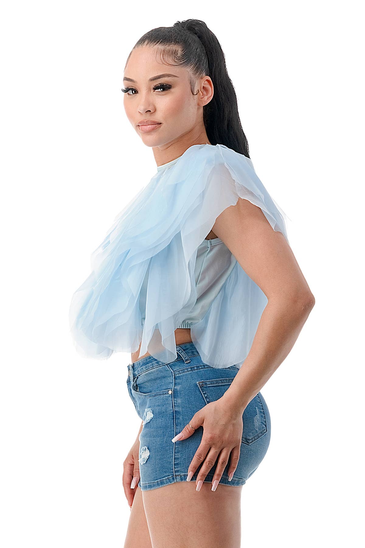 Woman wearing a light blue sheer top over a gray shirt with denim shorts on a white background