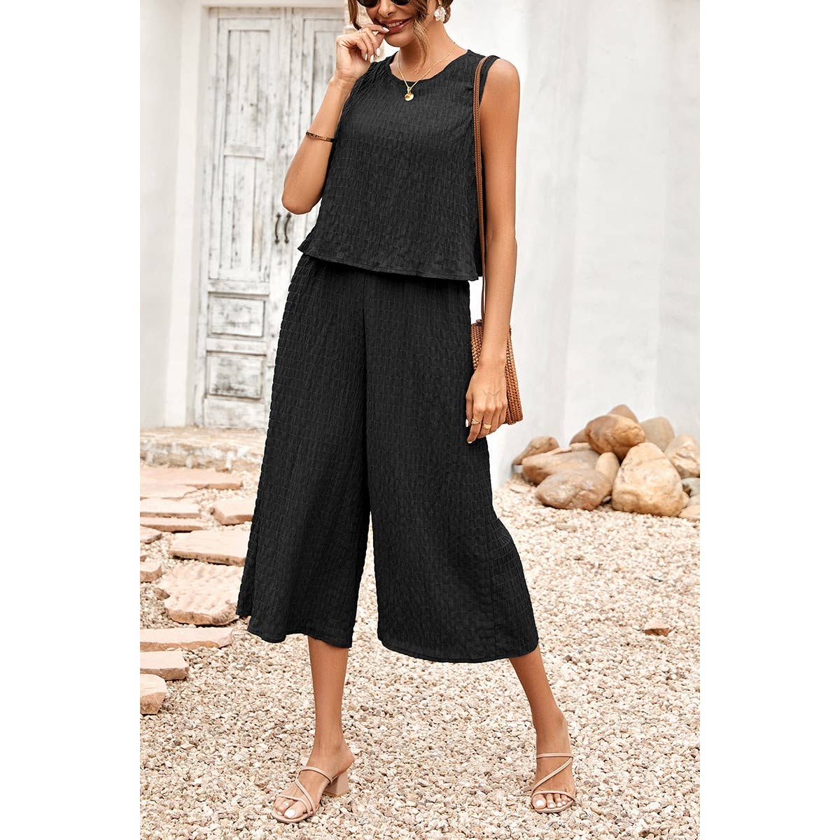 Woman wearing a black sleeveless top and wide-leg pants standing outdoors.