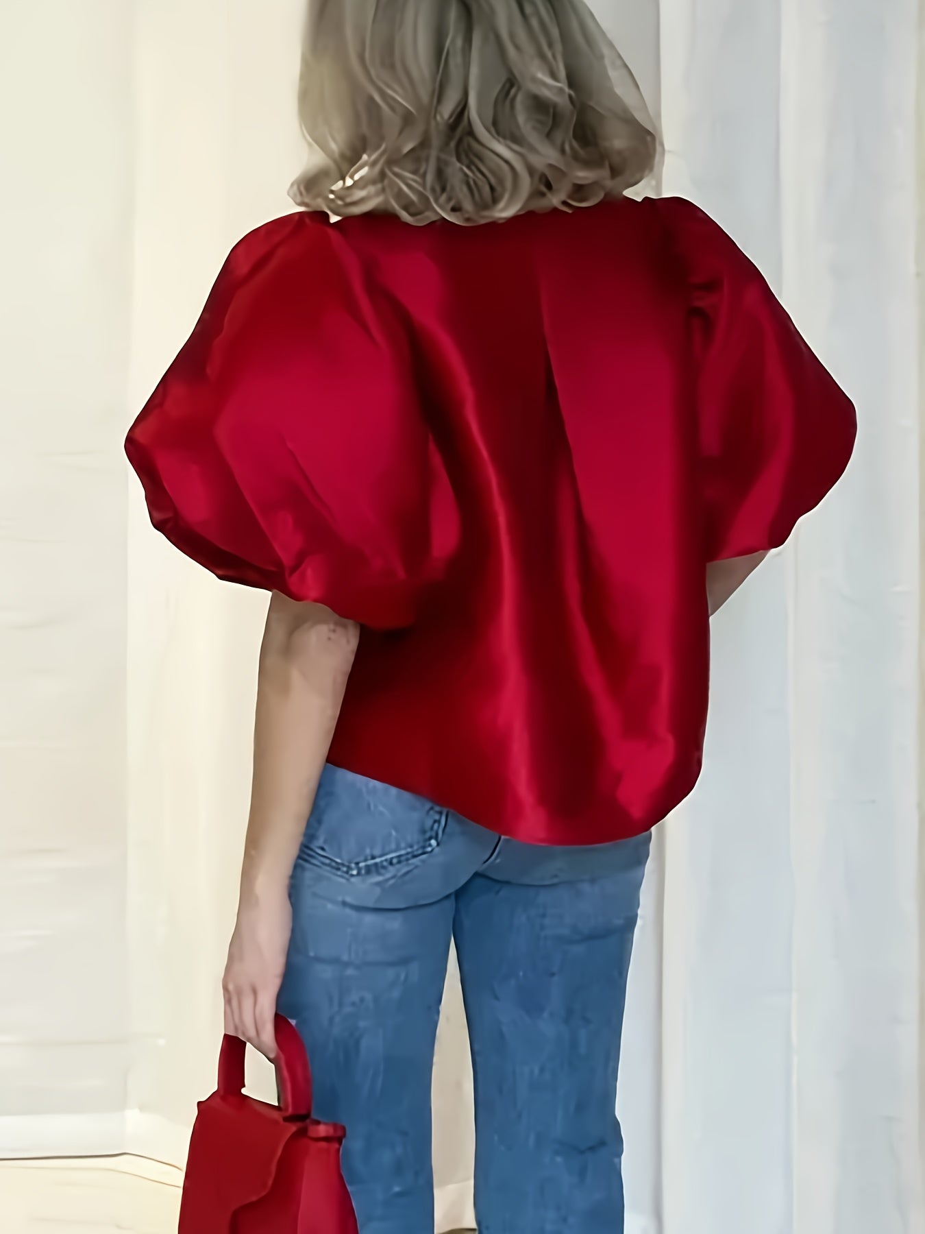 Person wearing a red satin top and blue jeans, holding a matching red handbag against a neutral background.
