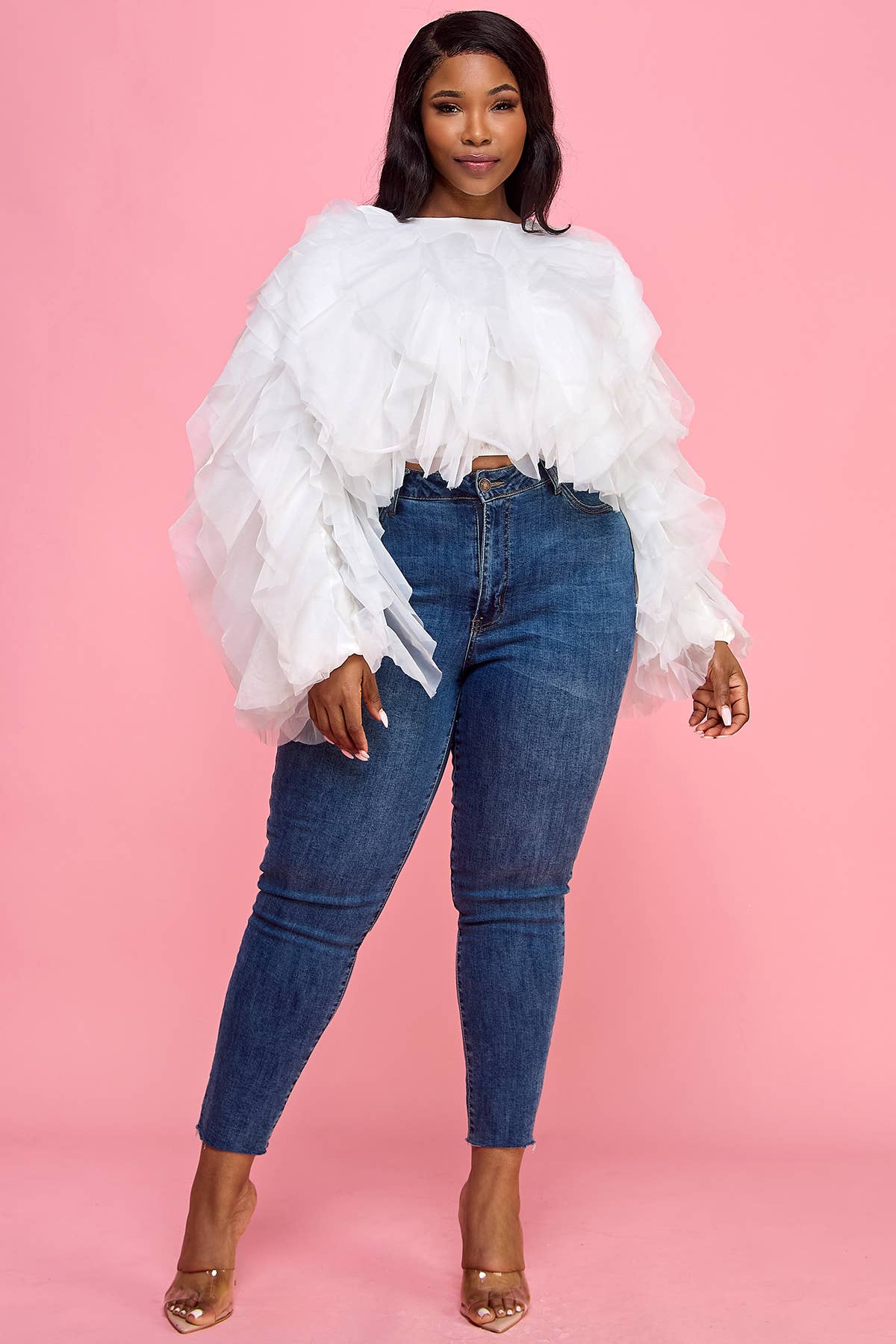 Woman wearing a white ruffled top and blue jeans against a pink background