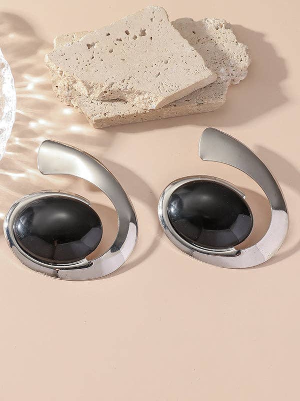 Pair of silver earrings with black stones on a beige surface