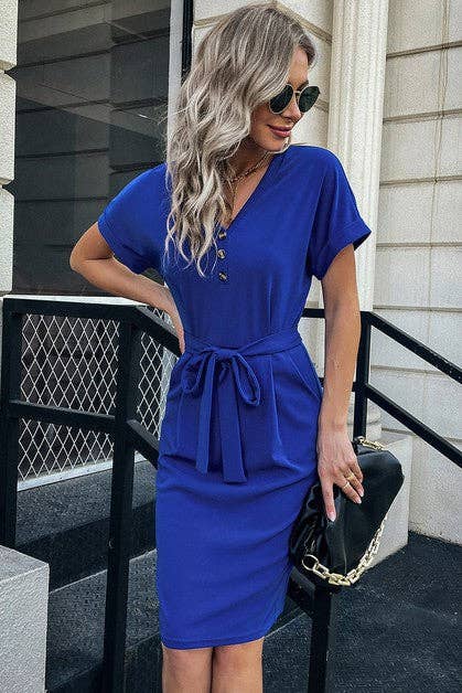 Woman wearing a blue dress with a black handbag on a city street.
