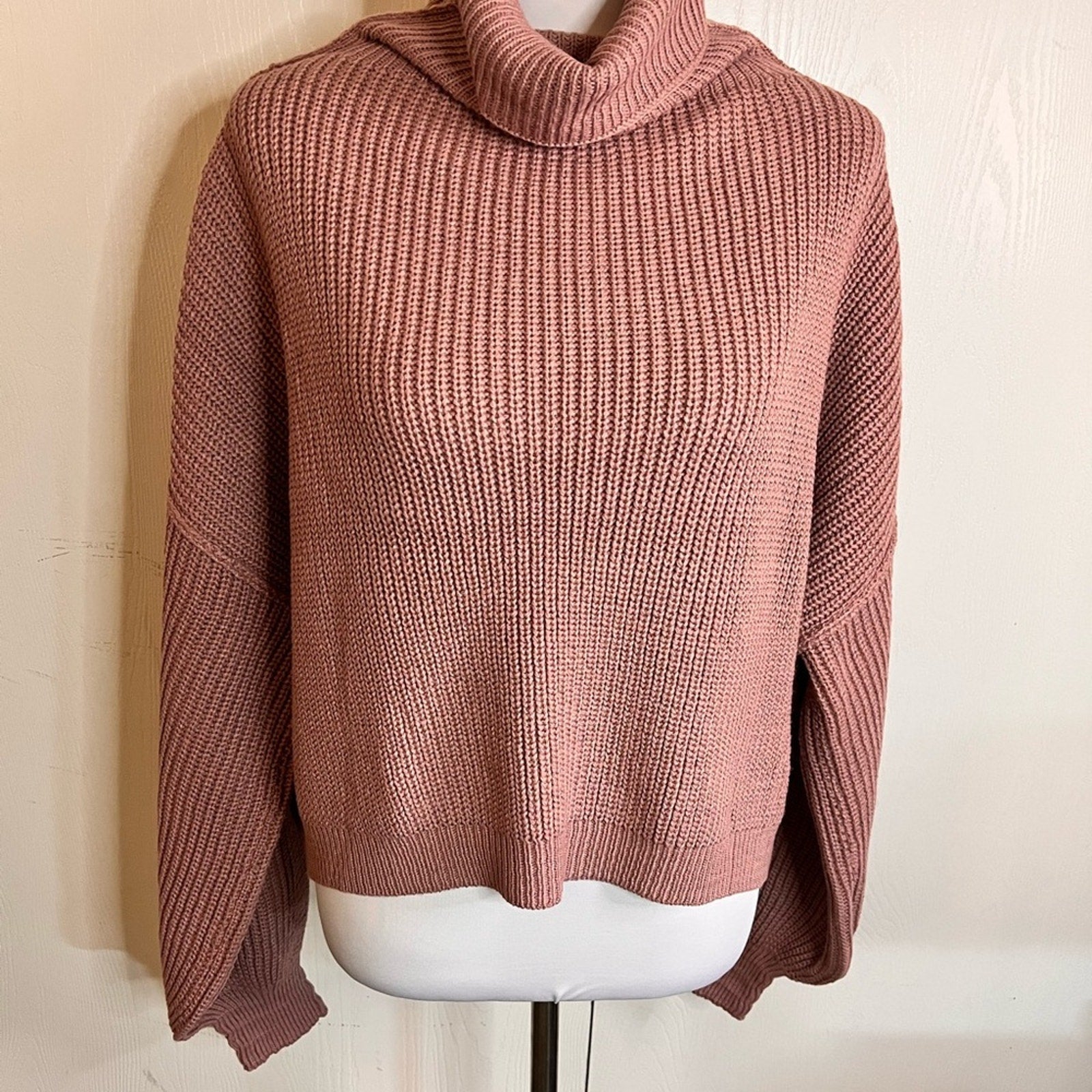 Pink knitted sweater on a mannequin against a beige wall