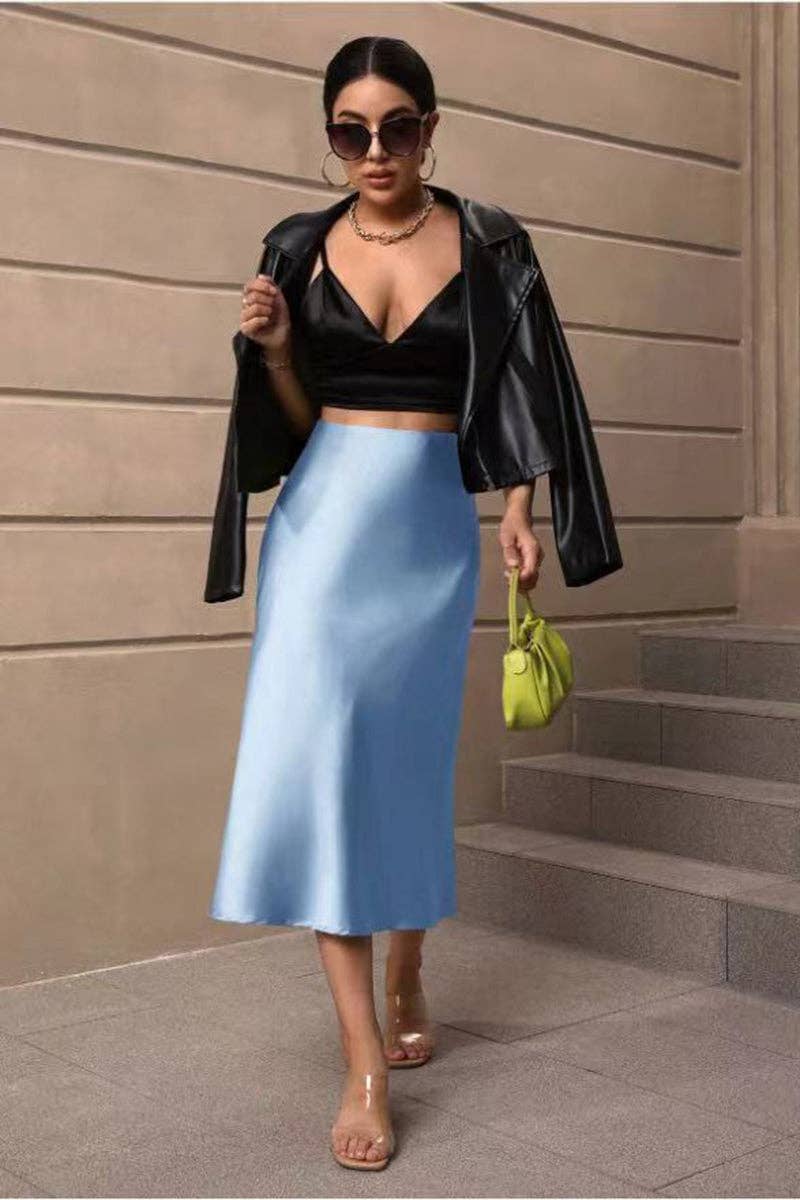 Woman in black leather jacket, black top, and blue skirt holding a green handbag on steps.