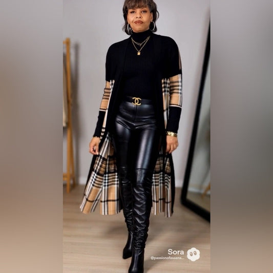 Woman wearing a black outfit with plaid sleeves and a long coat, standing indoors.