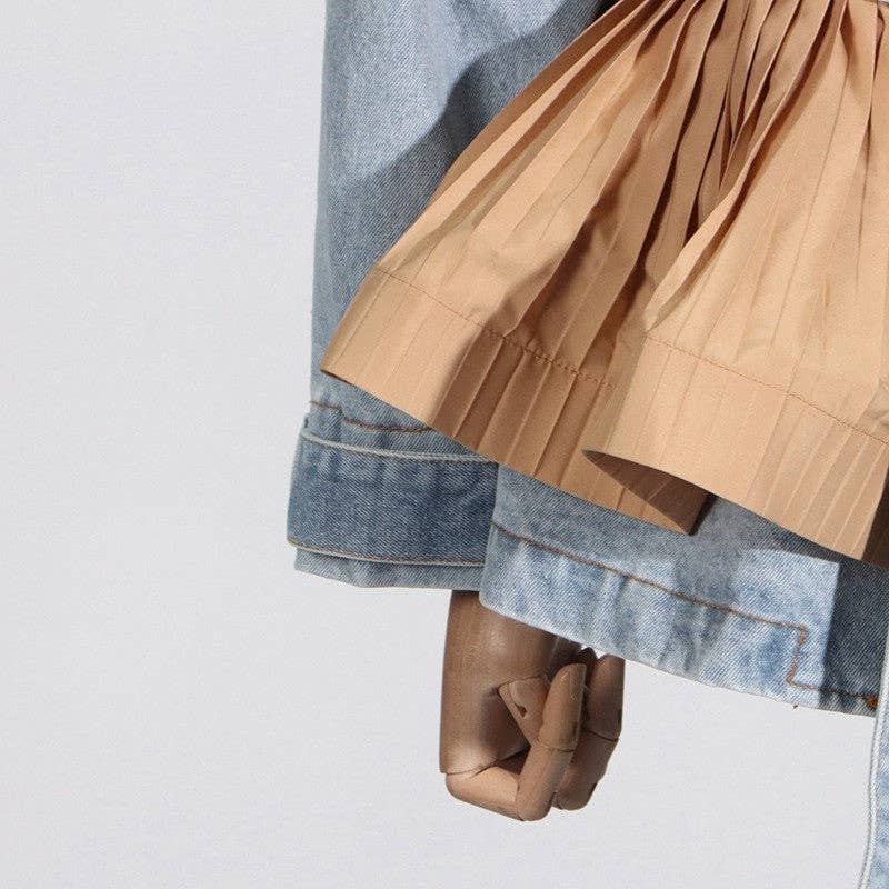 Close-up of a hand wearing a brown glove with a beige pleated skirt and blue denim jacket on a light gray background.