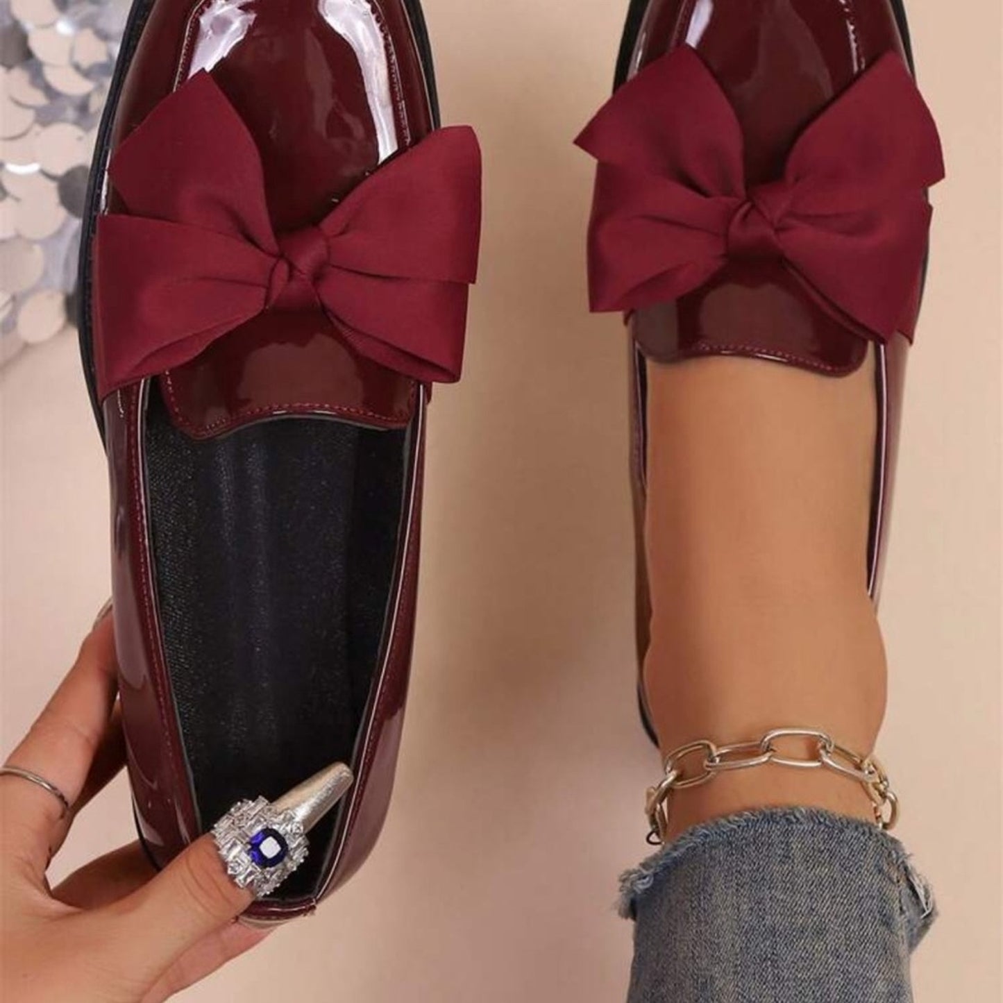 Burgundy loafers with large red bows worn by a person on a beige background