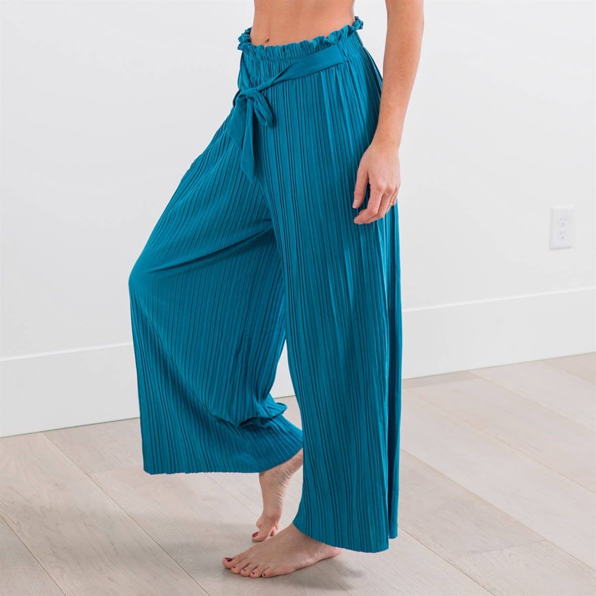 Person wearing teal pleated pants in a minimal indoor setting