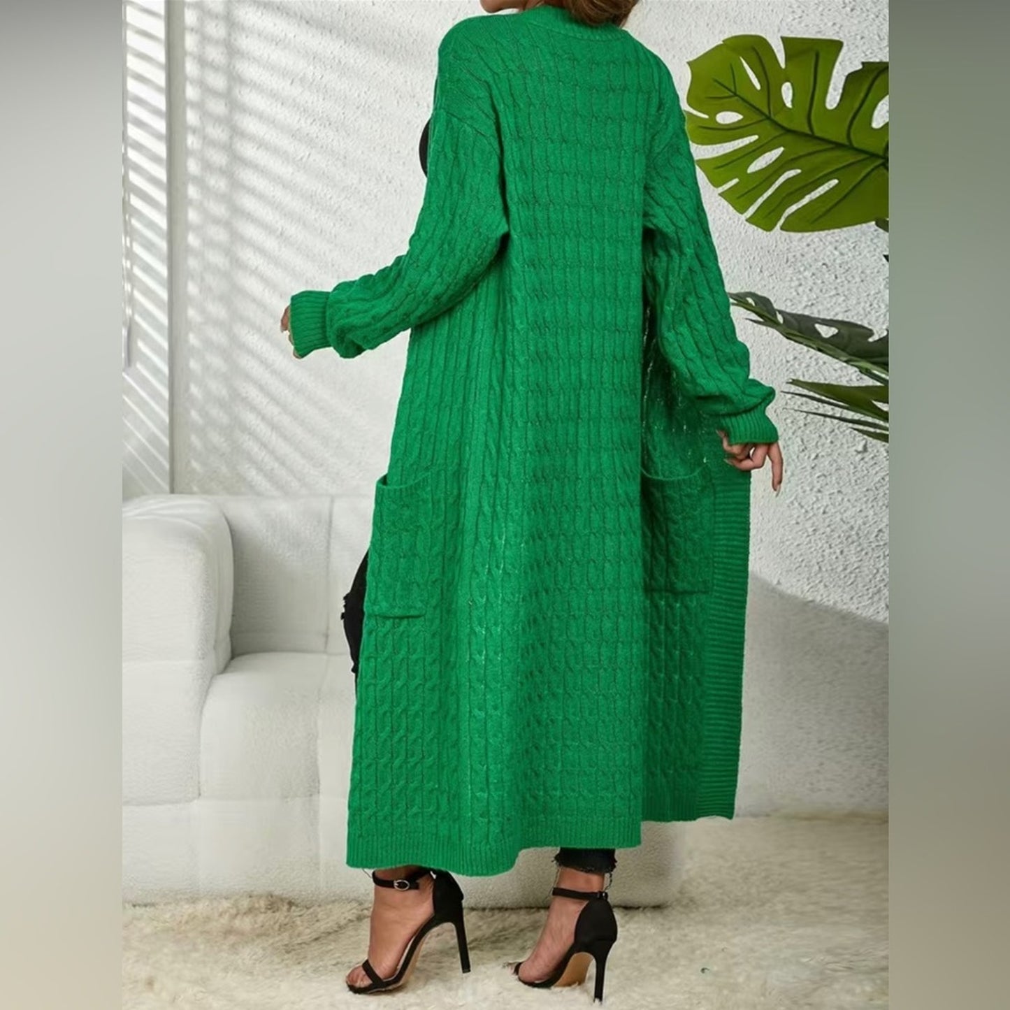 Person wearing a green cable knit dress in a room with white walls and a plant.