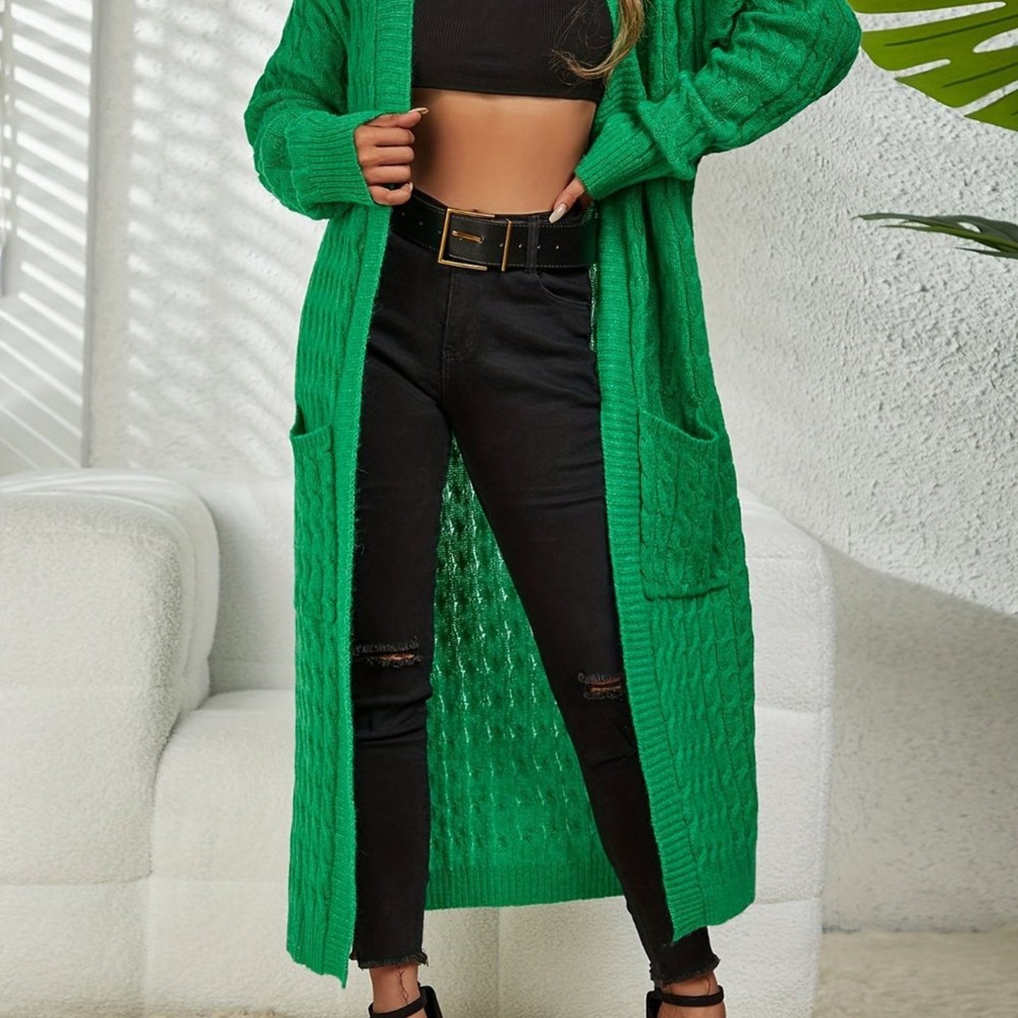 Person wearing a long green cardigan over a black outfit with a white background