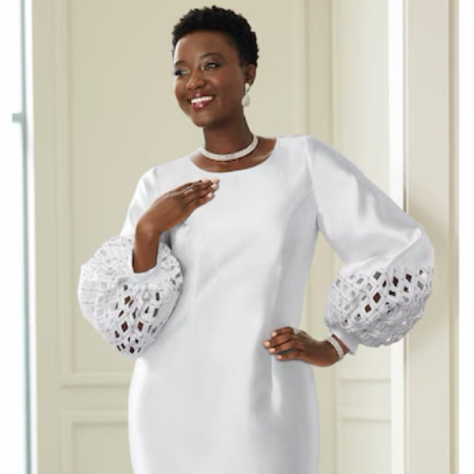 Woman wearing a white dress with lace sleeves against a neutral background