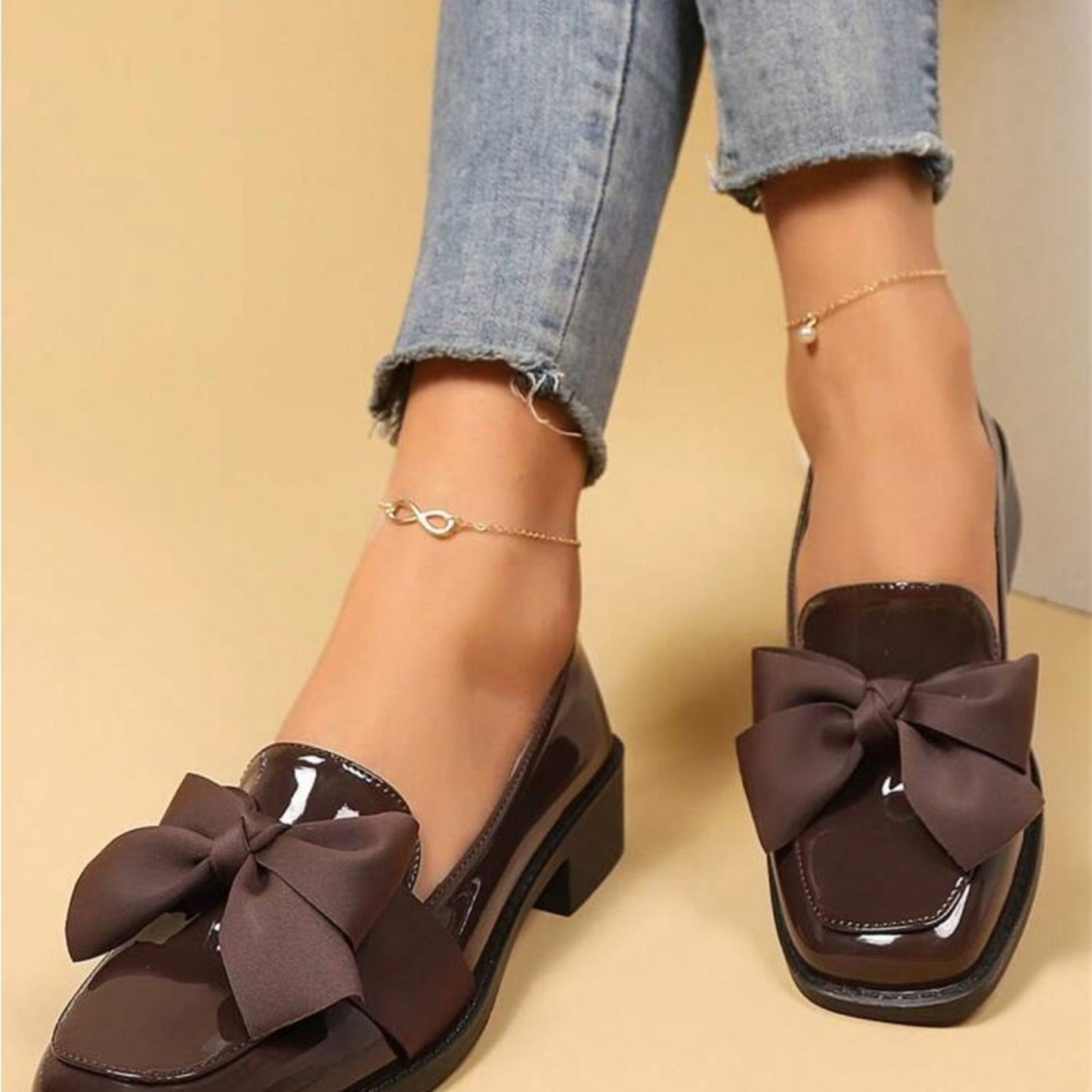 Brown shoes with large bows worn with rolled-up jeans on a beige background