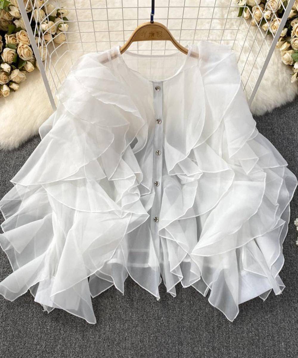 White ruffled blouse on a hanger with a floral and fur background