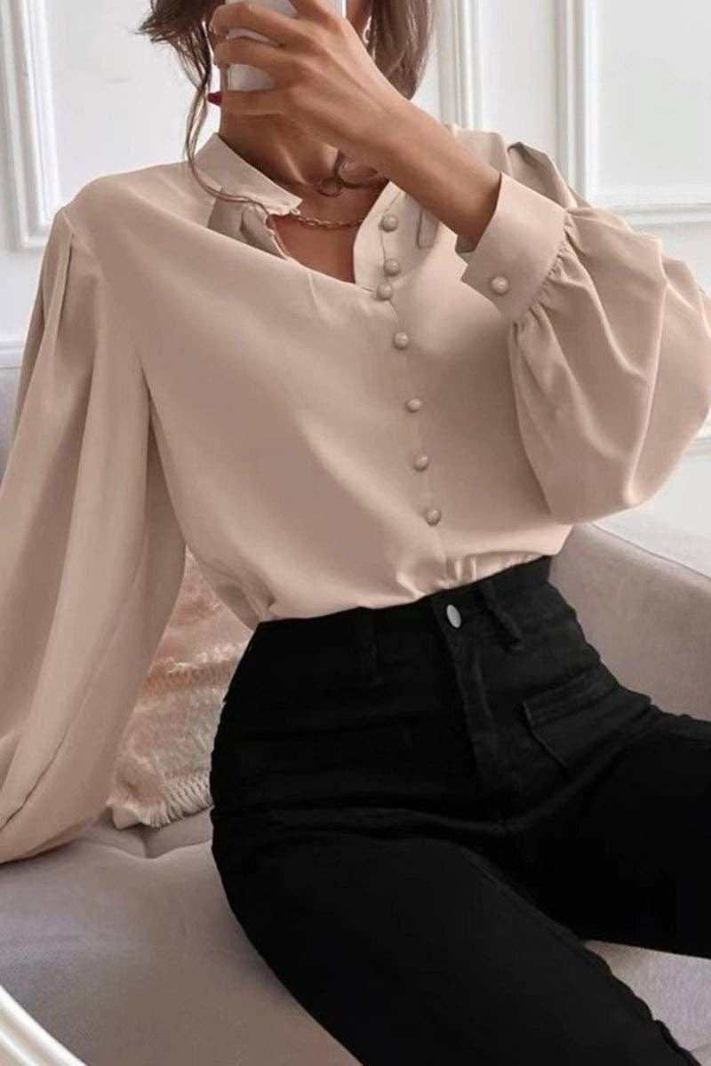 Person wearing a beige blouse with white buttons and black pants sitting on a couch.