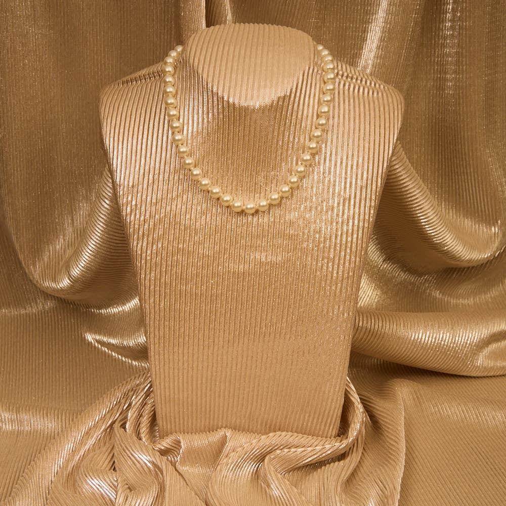 Mannequin wearing a beige dress with a pearl necklace against a gold fabric background