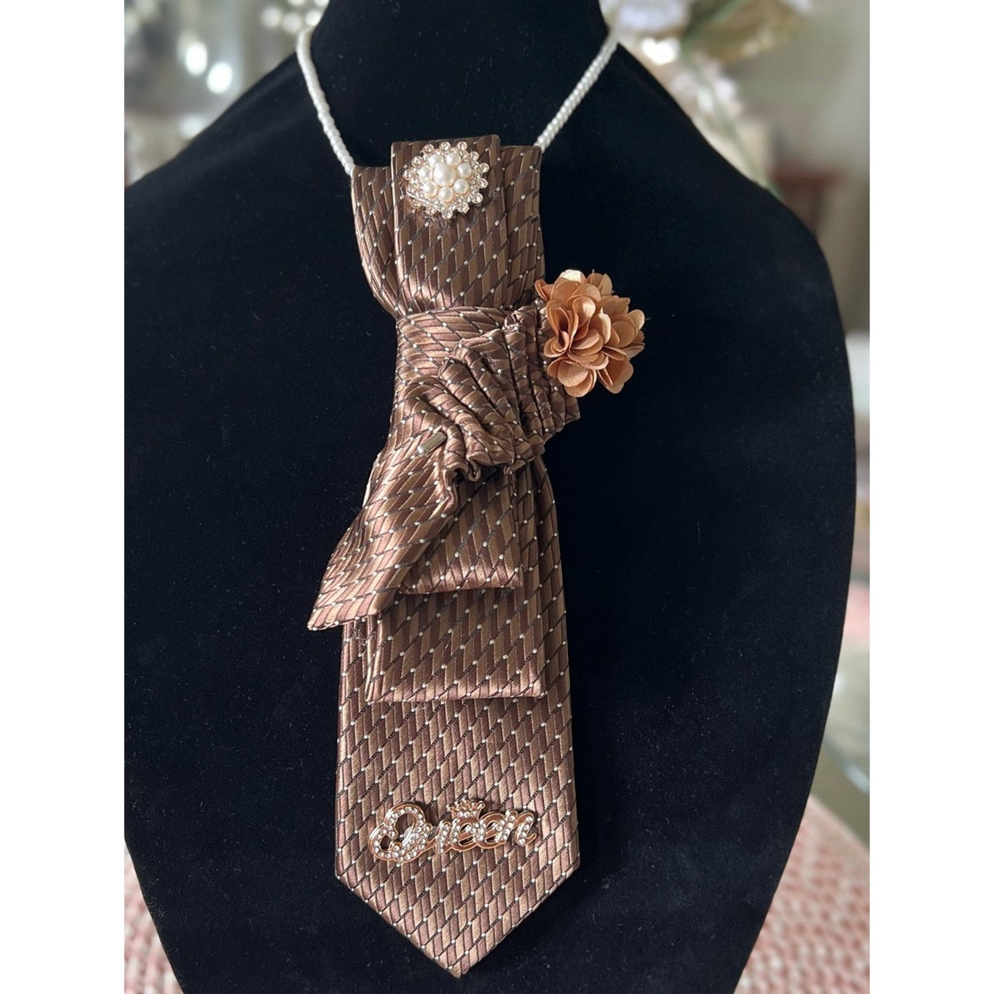 Bronze patterned tie with decorative elements on a black stand.