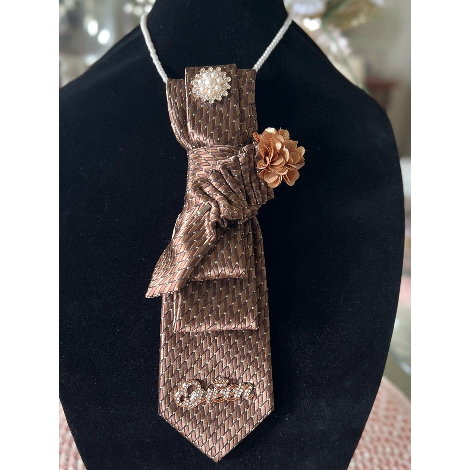 Bronze patterned tie with decorative elements on a black stand.
