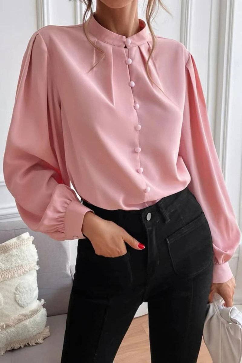 Person wearing a pink blouse with long sleeves and black pants indoors.