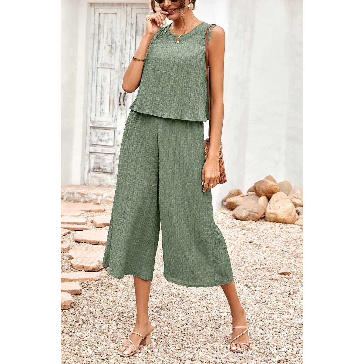 Woman wearing a green outfit standing outdoors with a white wall and stones in the background