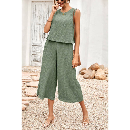 Woman wearing a green outfit standing outdoors with a white wall and stones in the background