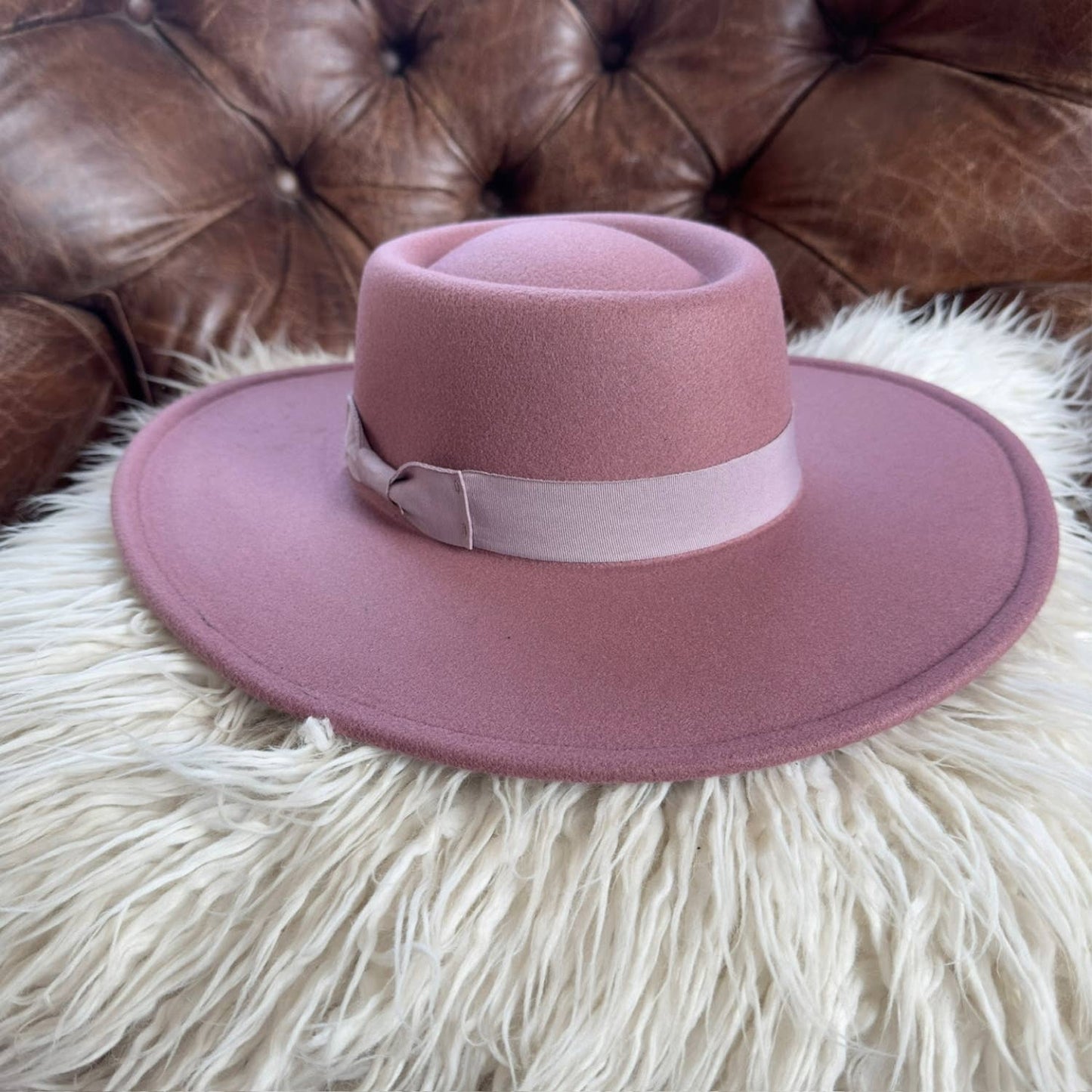 Pink hat with a wide brim on a fluffy white surface with a brown leather couch in the background.