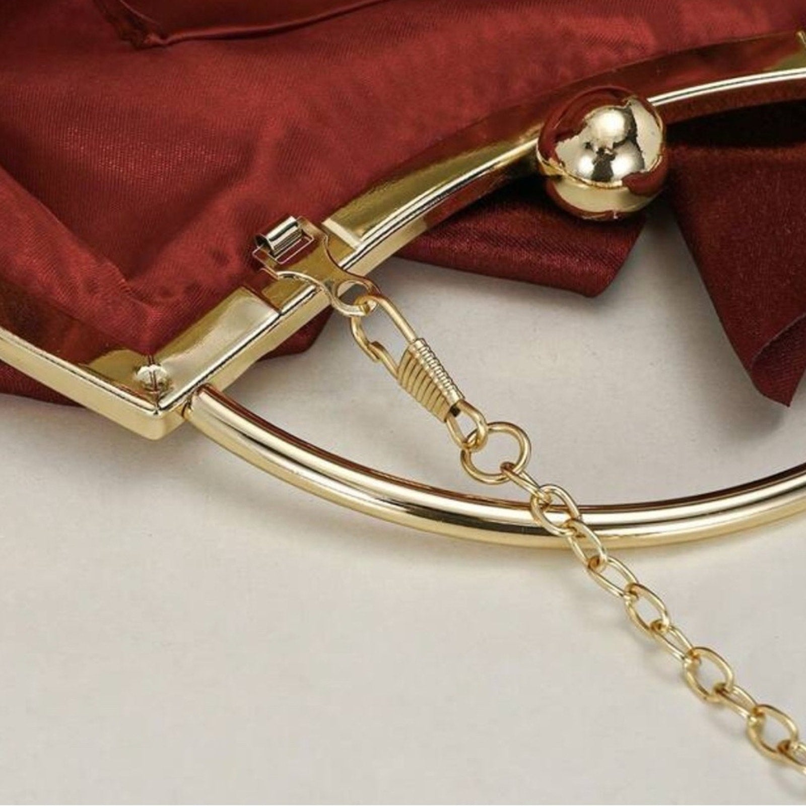 Close-up of a gold clutch with a chain detail on a red fabric background