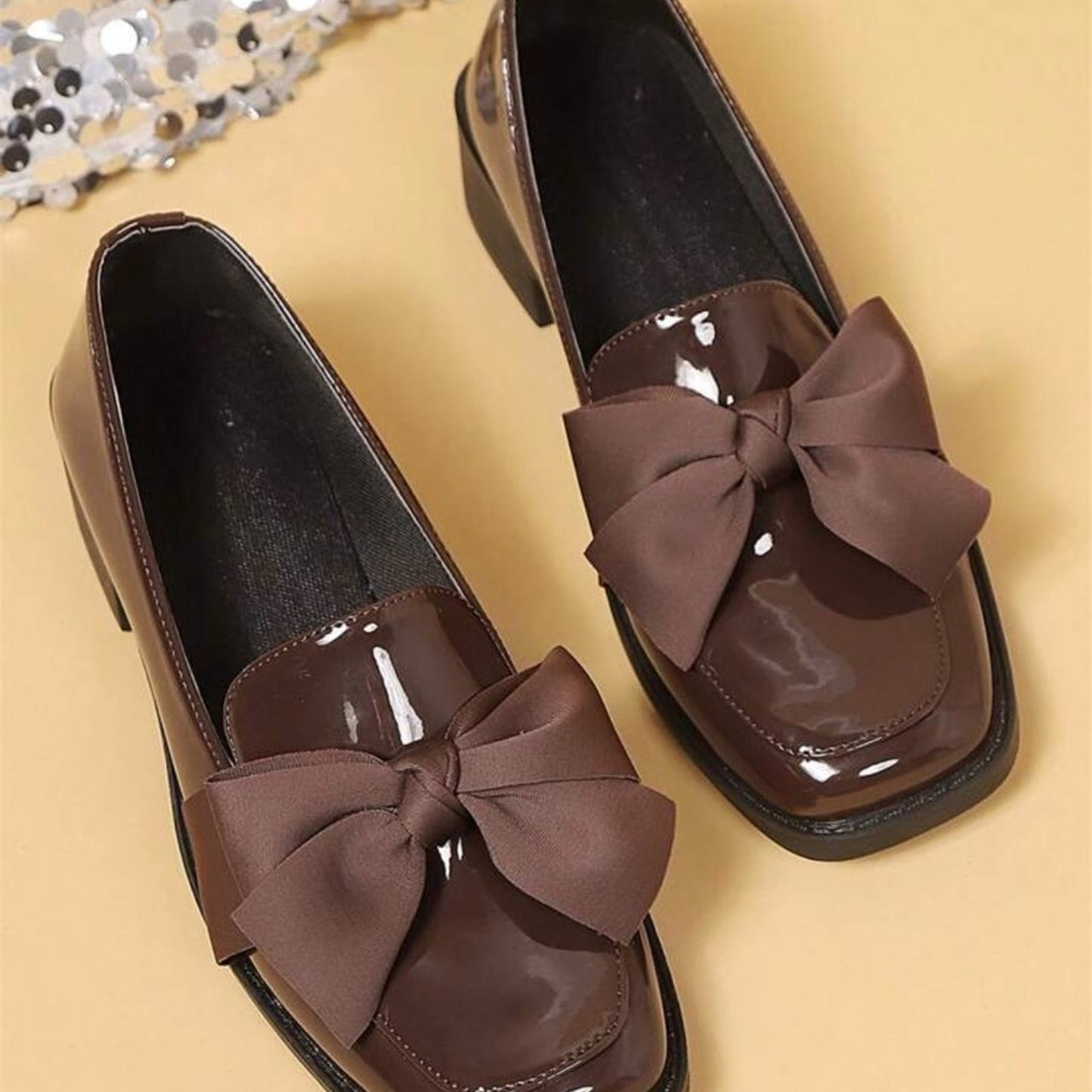 Brown patent leather shoes with large bows on a beige background