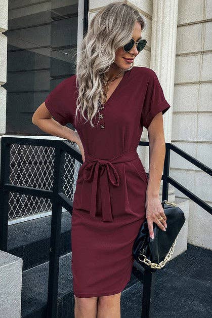Woman wearing a burgundy dress with a black handbag on a staircase.