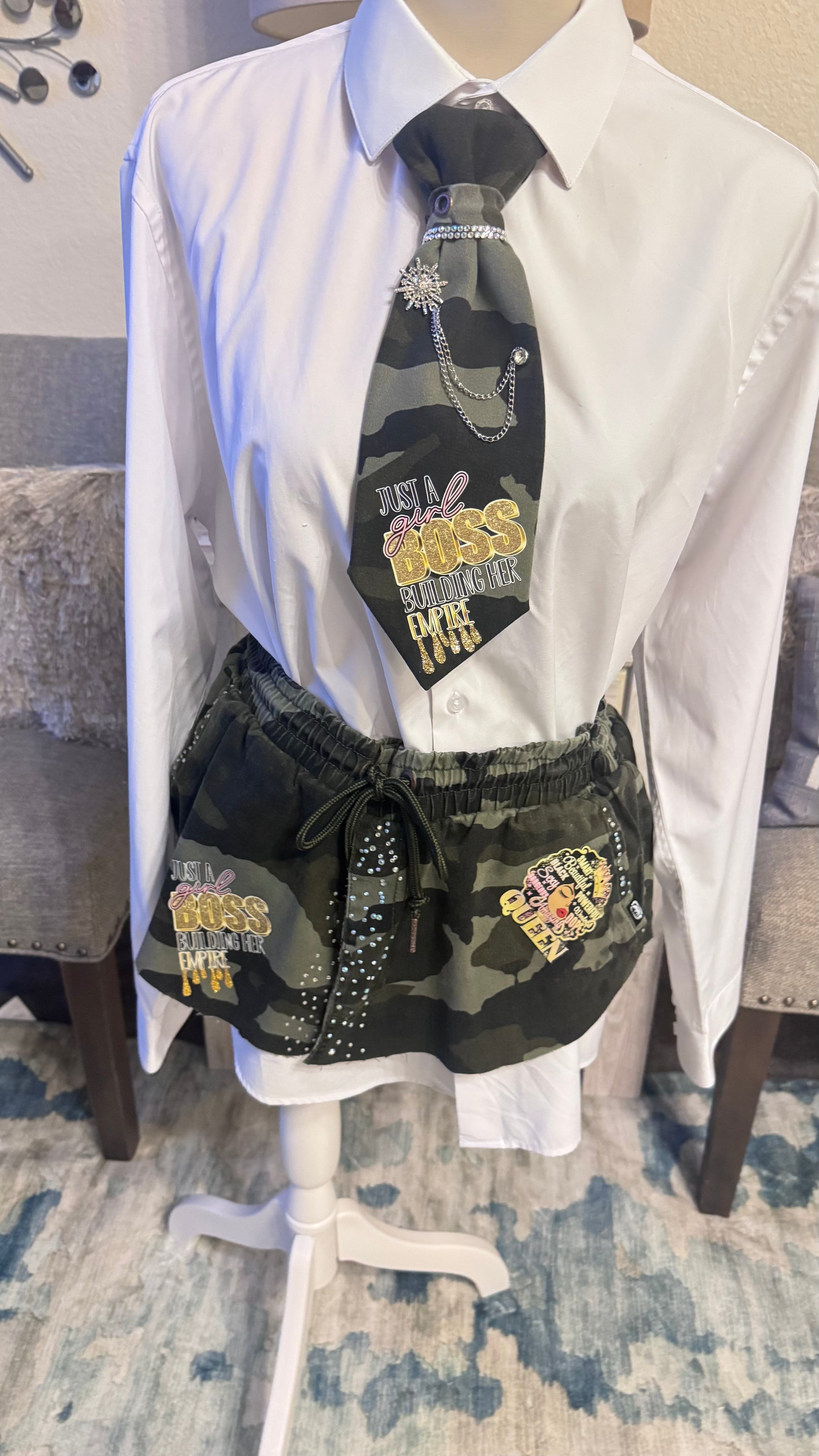 Mannequin wearing a white shirt, black tie with text, and camouflage shorts with patches.