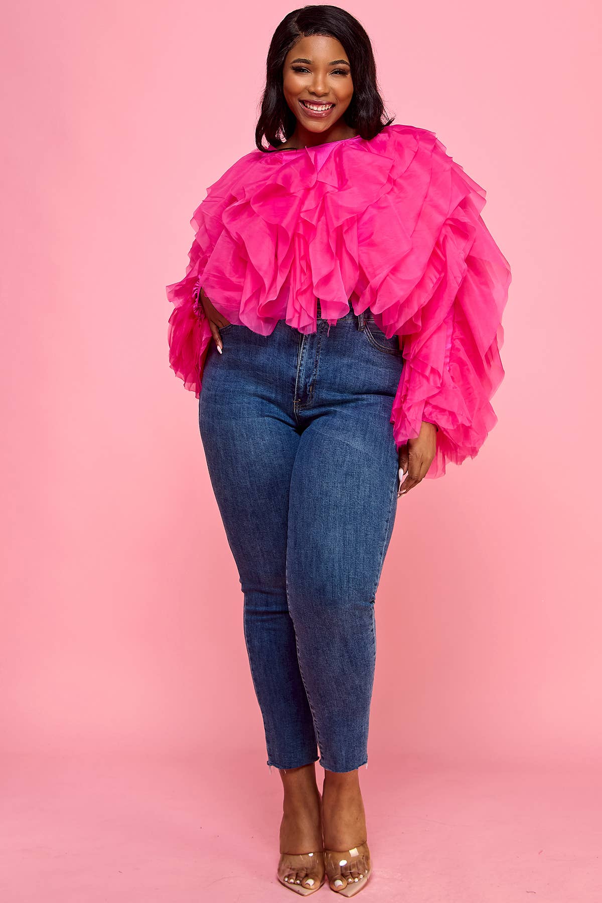 Woman wearing a bright pink ruffled top and blue jeans on a pink background