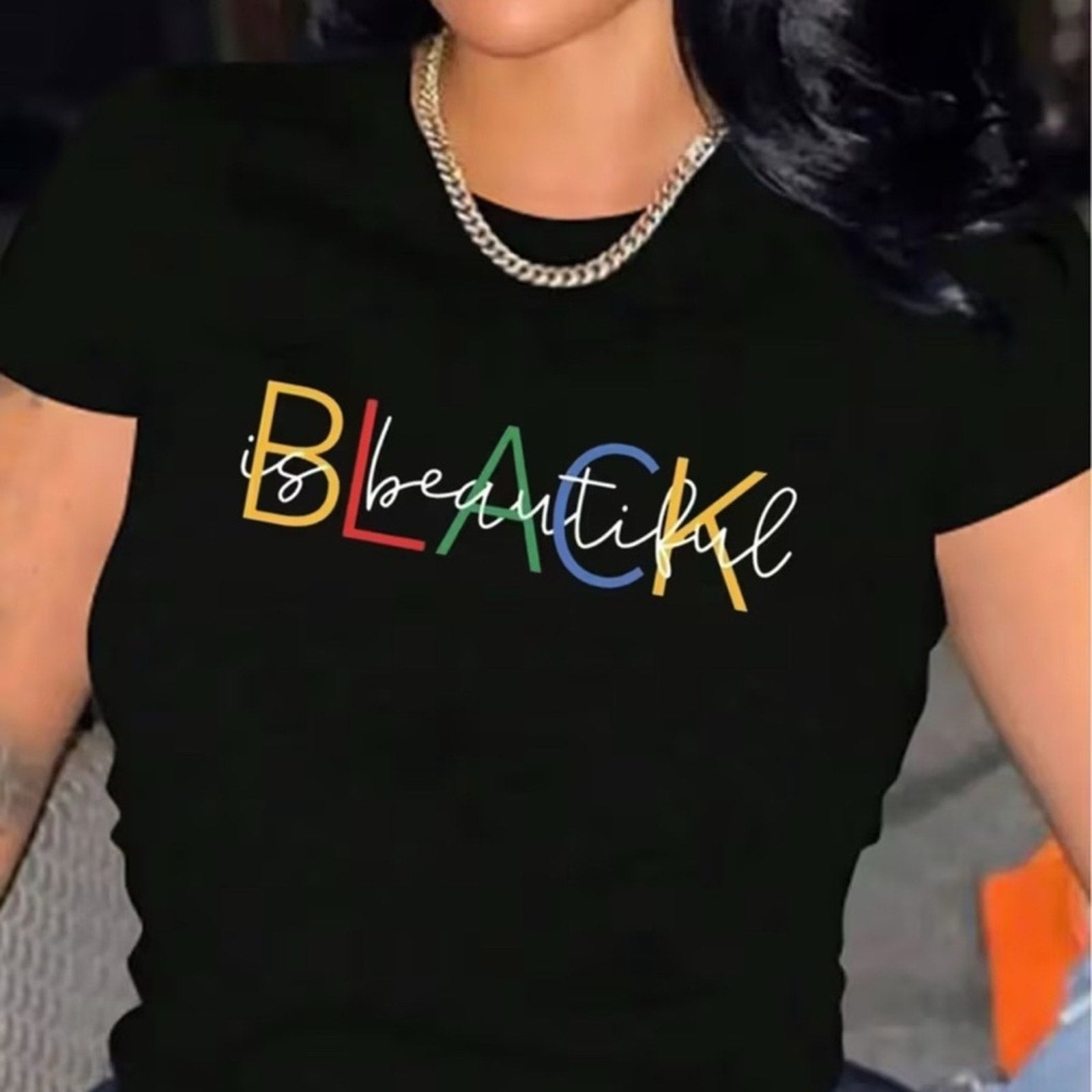 Black t-shirt with 'BLACK is beautiful' text in colorful letters worn by a person.