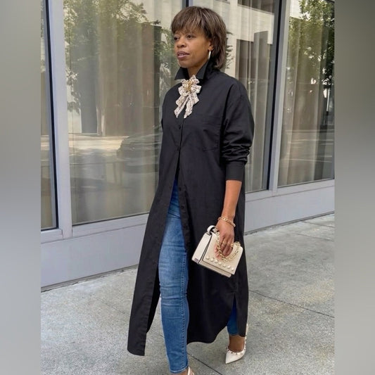 Woman wearing a black coat and blue jeans standing in front of a building.