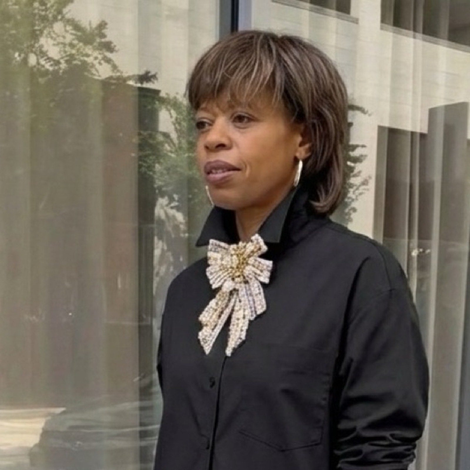 Woman wearing a black shirt with a large decorative bow standing in front of a glass wall.