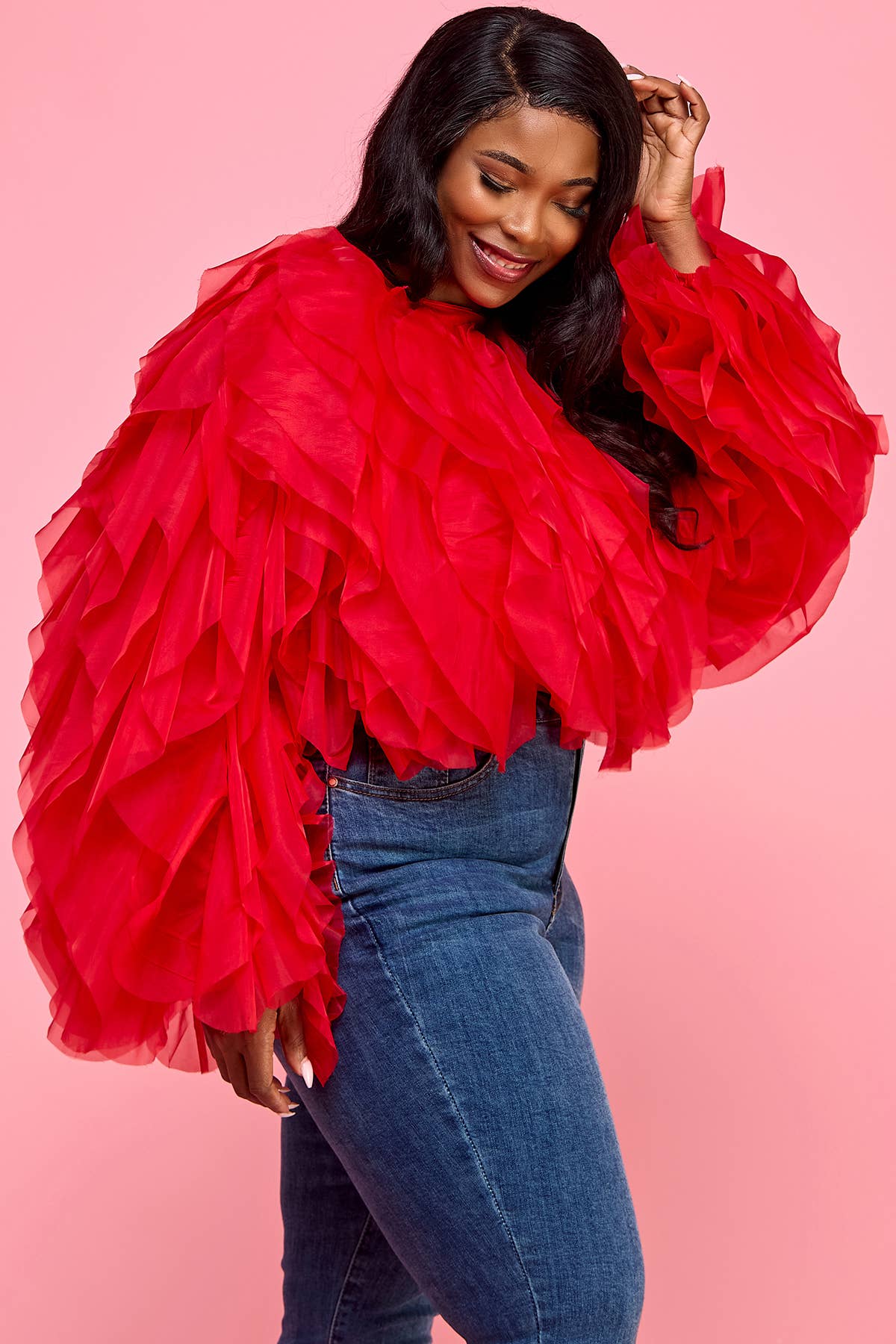 Woman wearing a red ruffled top and blue jeans on a pink background