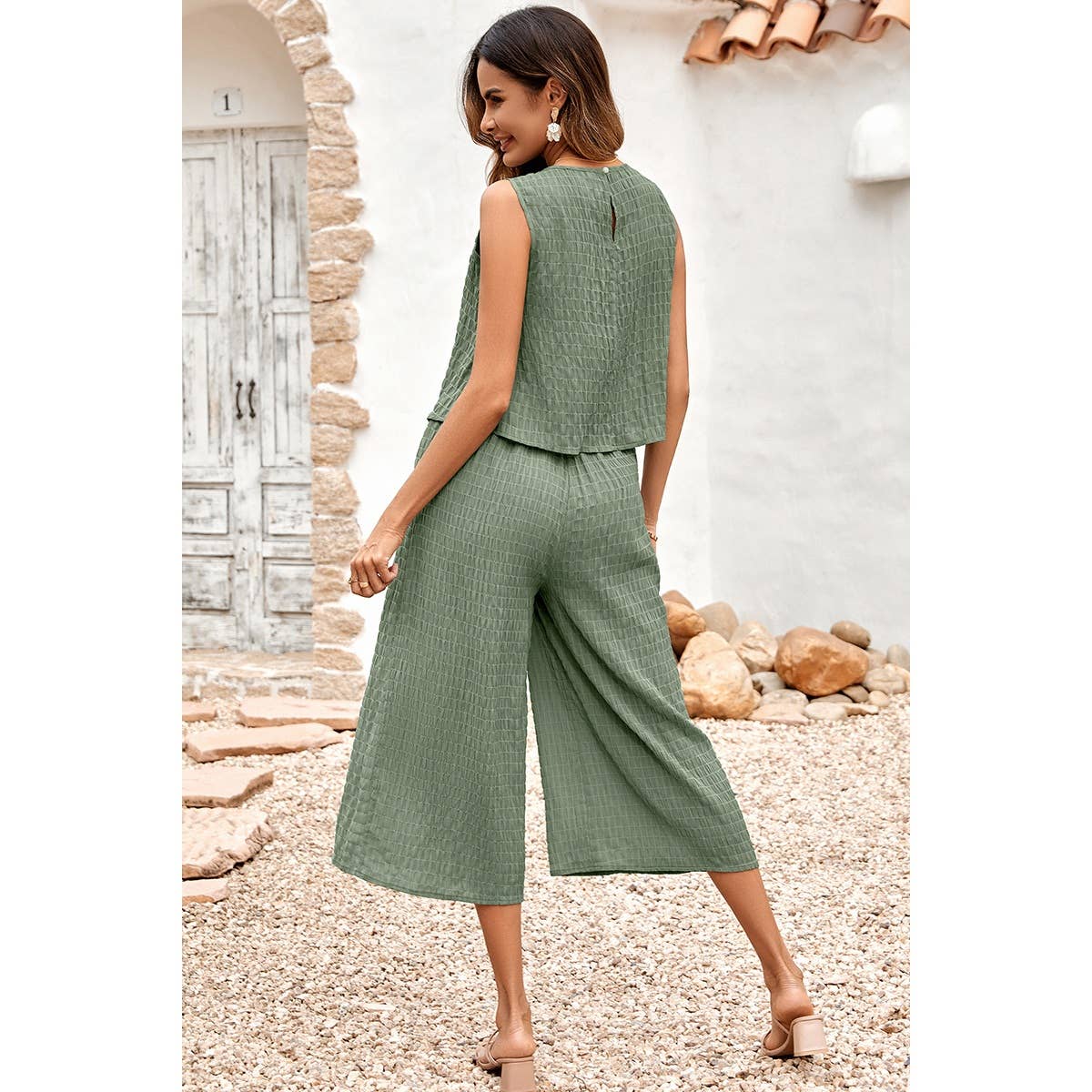 Woman wearing a green outfit standing in front of a stone wall and pebbles.