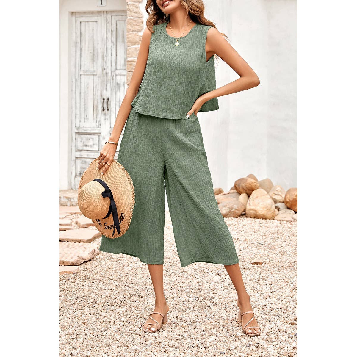 Woman in a green outfit holding a straw hat against a rustic background
