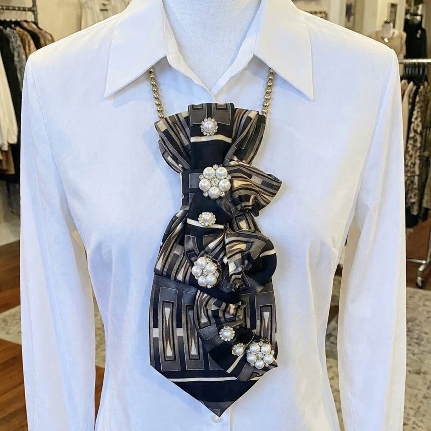 Mannequin wearing a white shirt with a decorative black and gold tie featuring pearls.