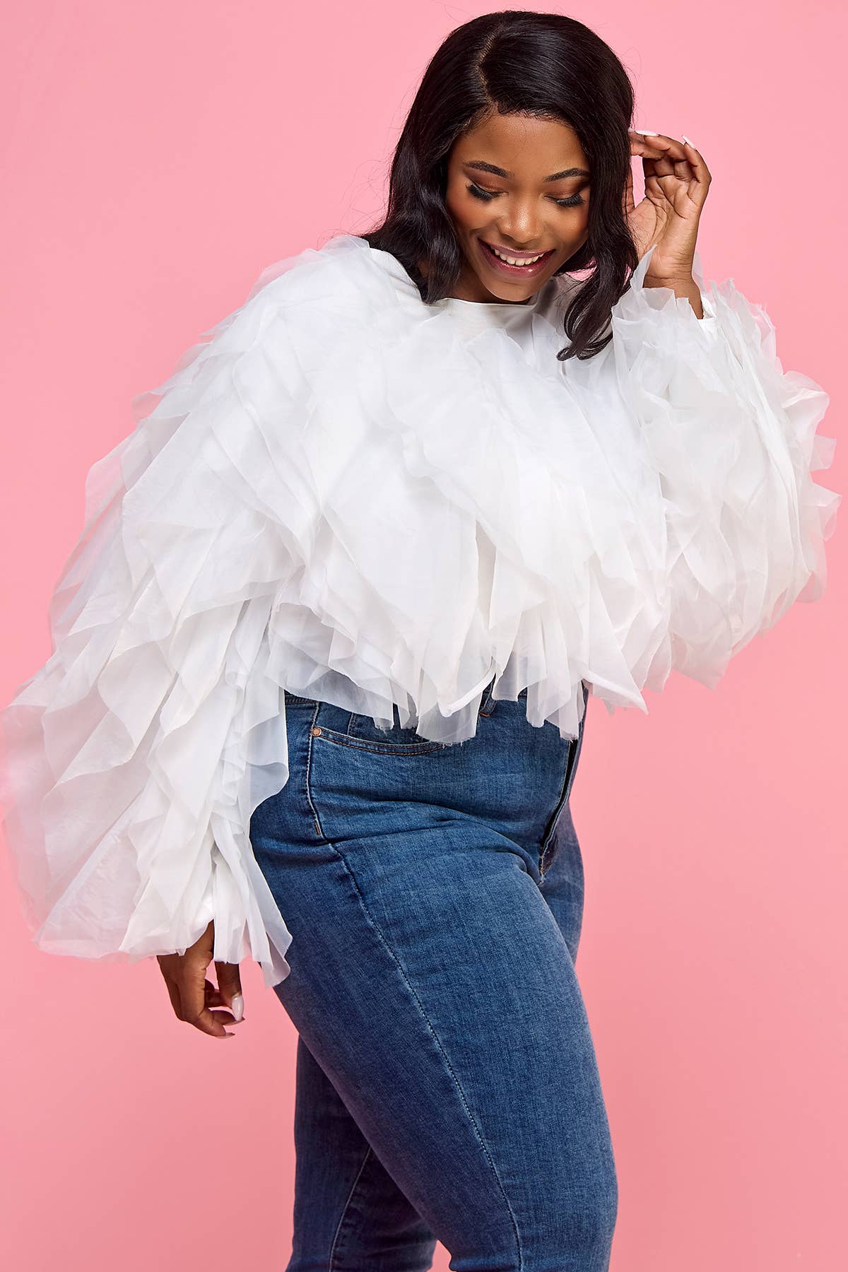 Woman wearing a white ruffled top and blue jeans against a pink background