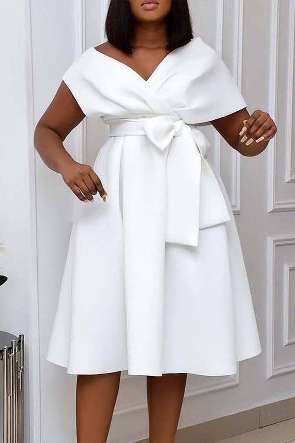 A woman wearing a black V-neck pleated waist strap dress with short sleeves and a bow detail at the front.