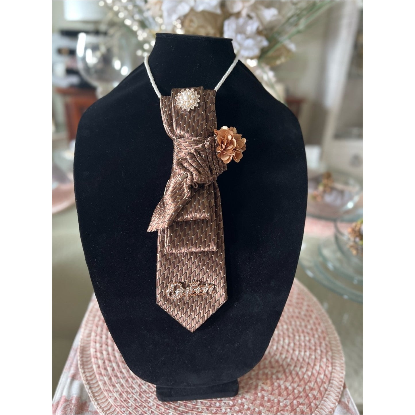 Brown textured tie with decorative elements on a black stand
