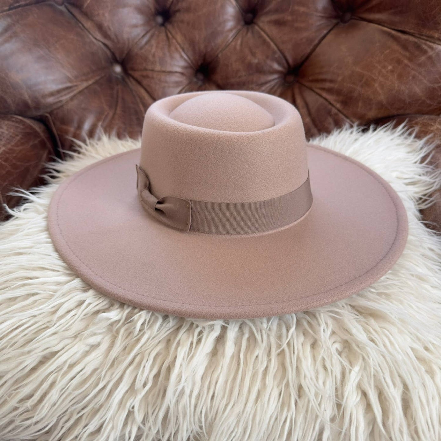 Brown fedora hat on a fluffy white surface with a brown leather couch in the background
