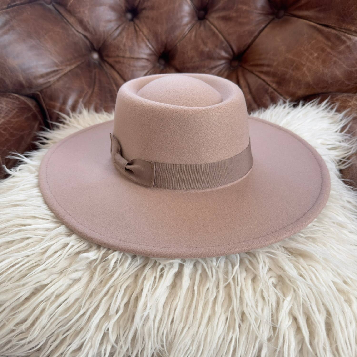 Brown fedora hat on a fluffy white surface with a brown leather couch in the background