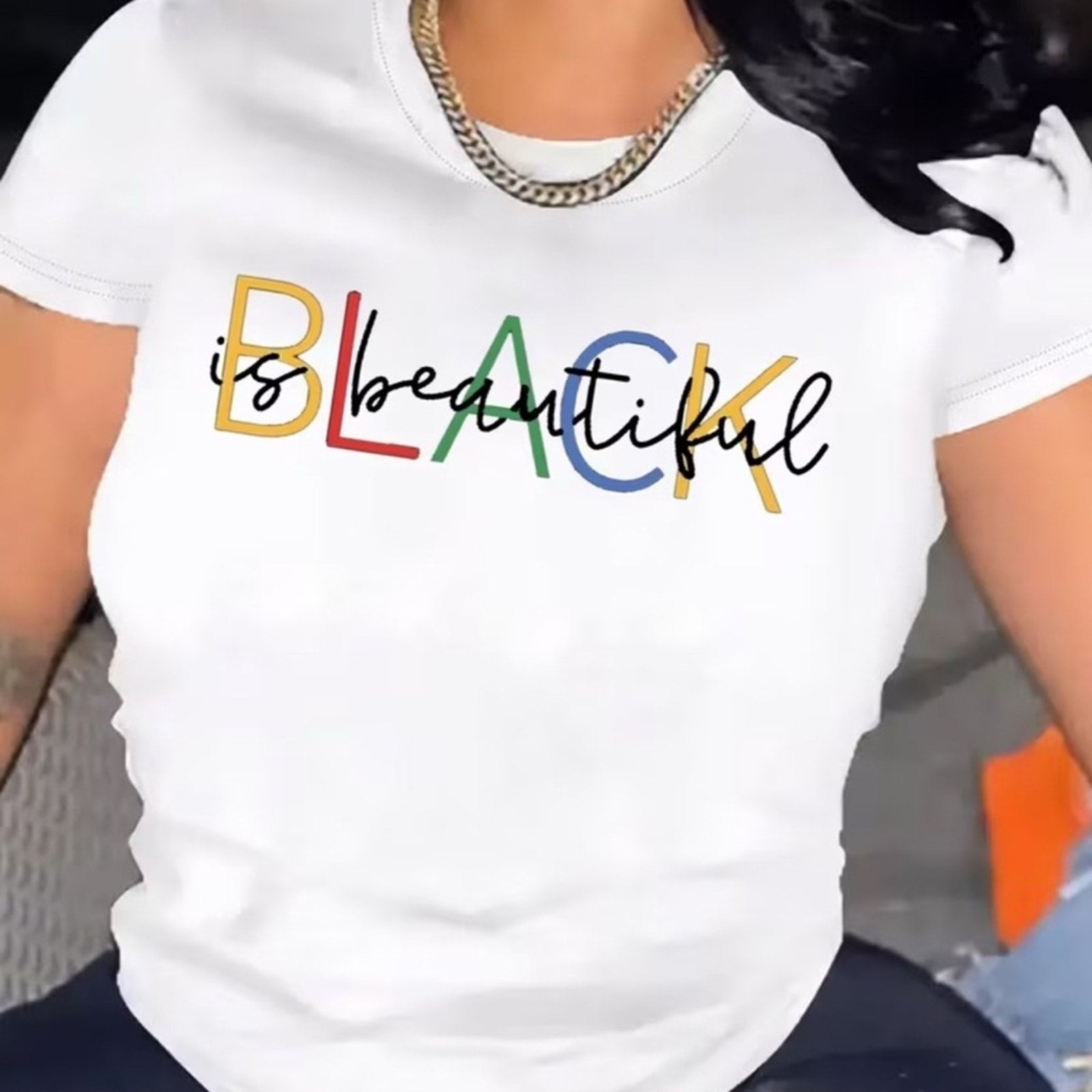 White t-shirt with 'Black is Beautiful' text in colorful letters worn by a person.
