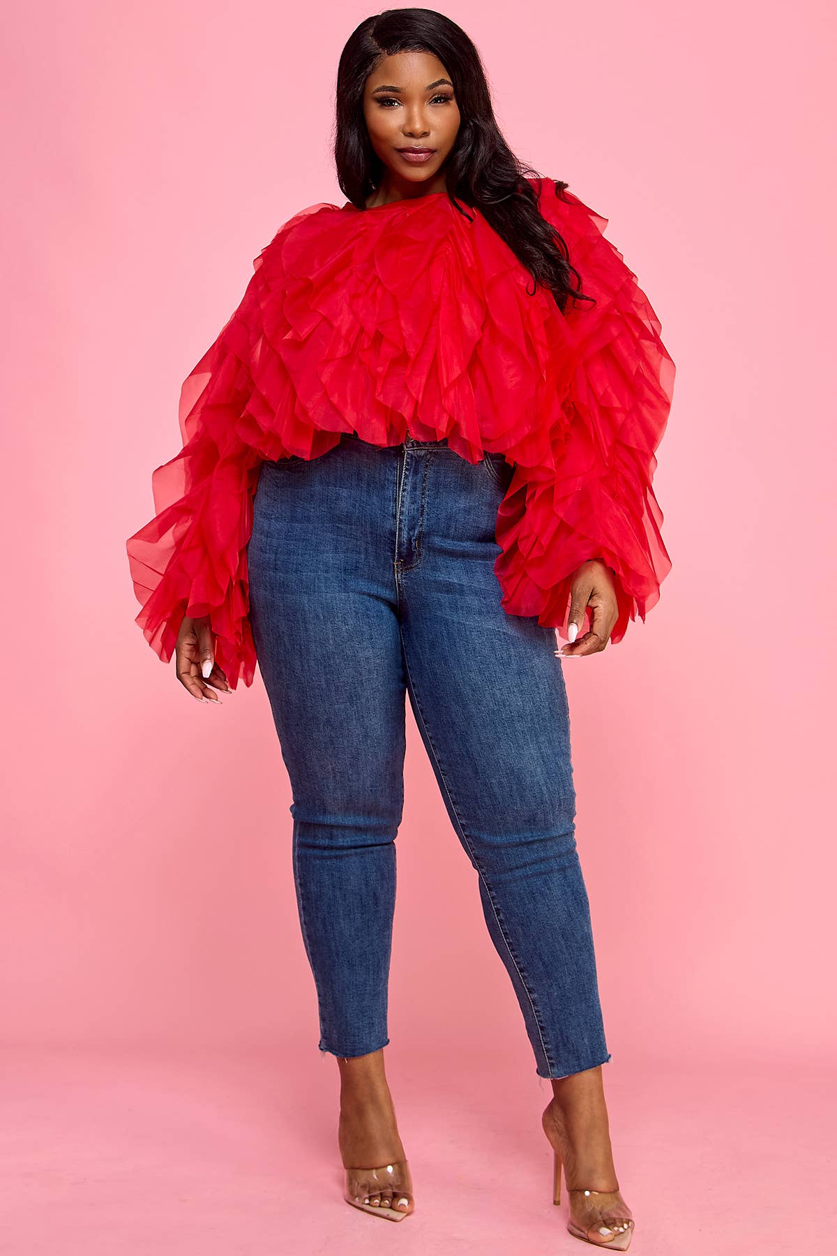 Woman wearing a red ruffled top and blue jeans on a pink background