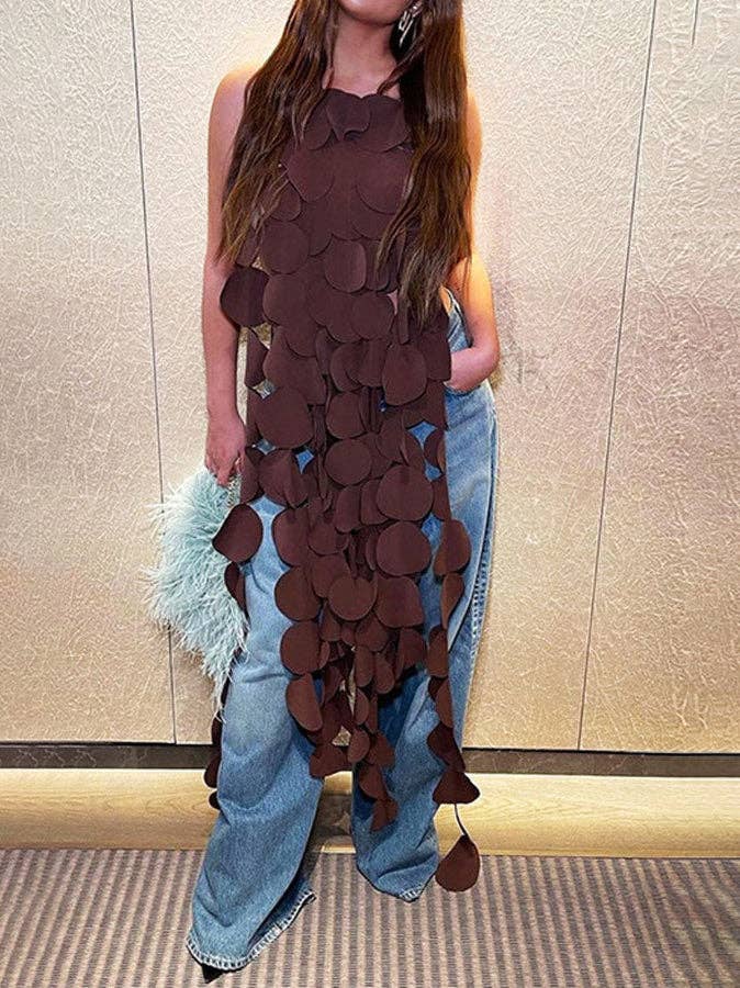 Person wearing a brown leaf-patterned dress with blue jeans against a neutral wall.