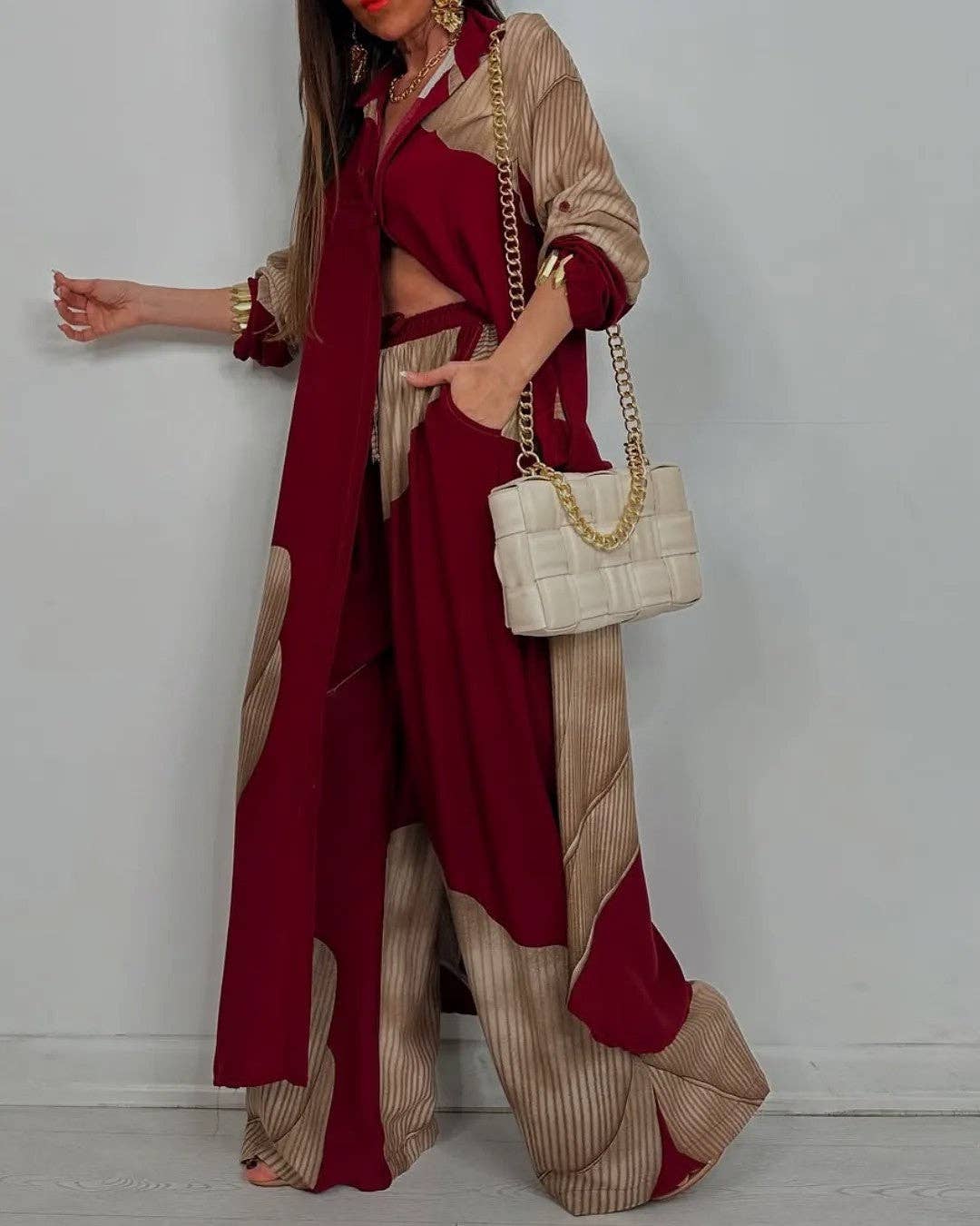 Person wearing a red and beige outfit with a white handbag against a plain background