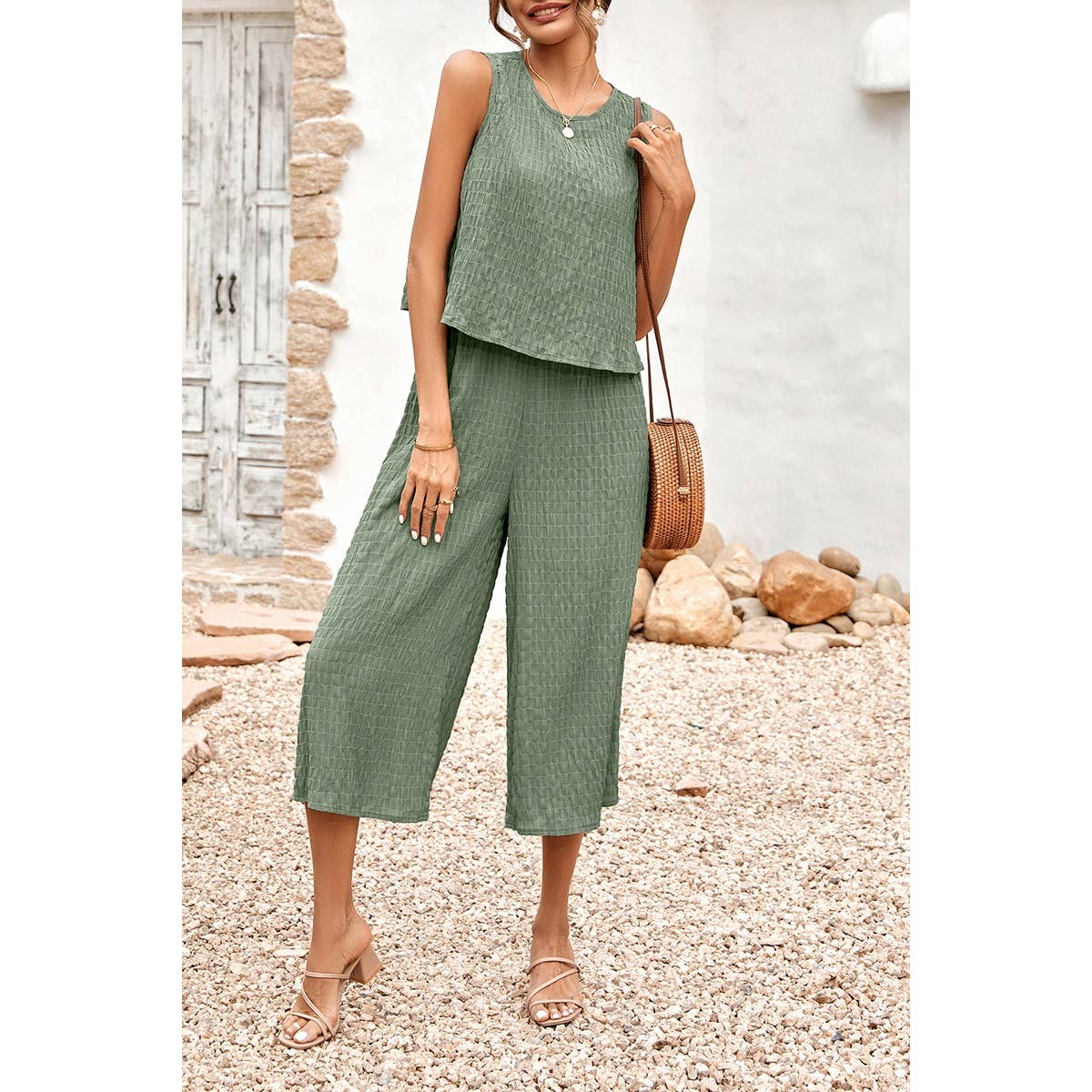 Woman wearing a green outfit standing outdoors with a stone wall and pebbles in the background.