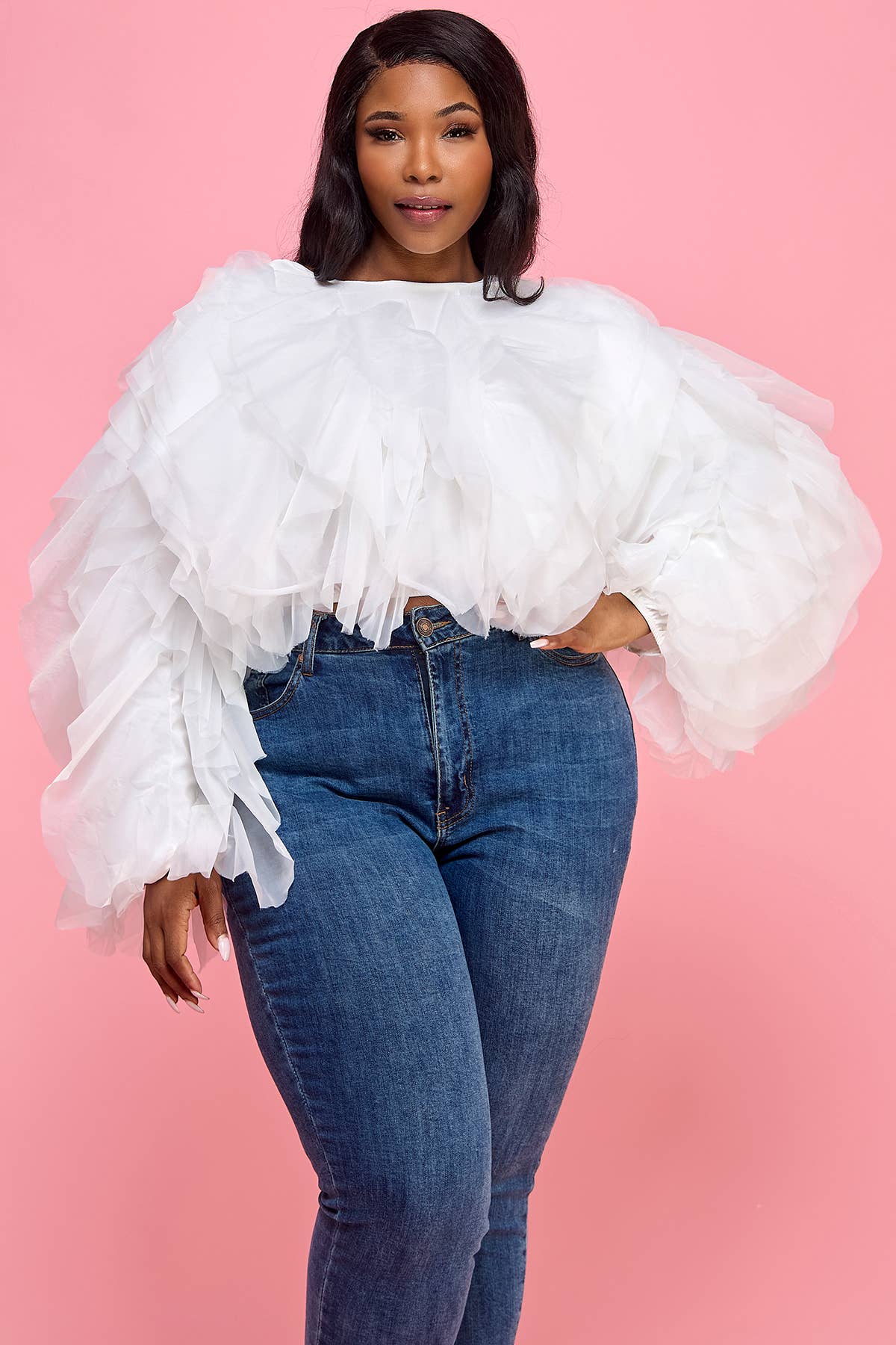 Woman wearing a white ruffled blouse and blue jeans against a pink background