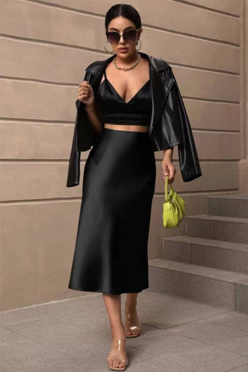 Woman in black outfit with green handbag standing on steps against a beige wall.