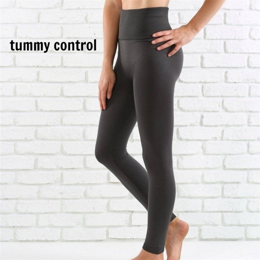 Person wearing gray leggings with 'tummy control' text on a white brick wall background